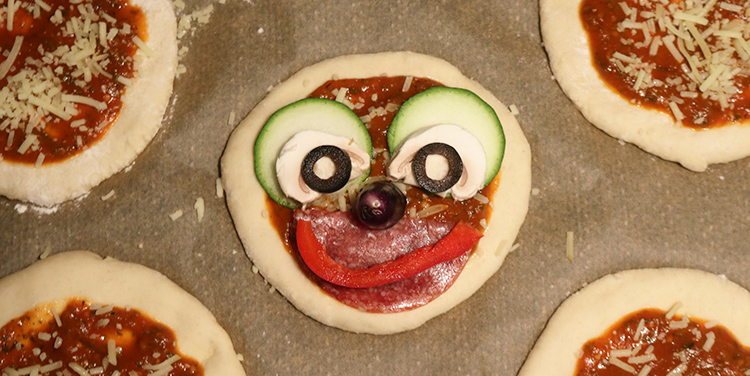 Pizzetten mit Gemüse zu Gesichtern legen