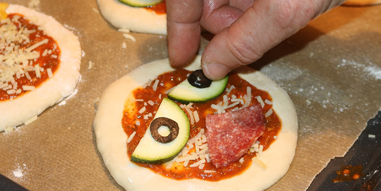 Pizzetten mit Gemüse zu Gesichtern legen