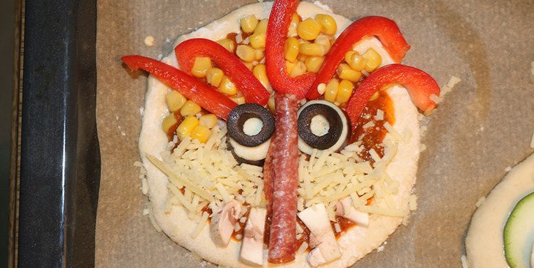 Pizzetten mit Gemüse zu Gesichtern legen