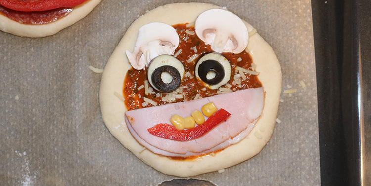 Pizzetten mit Gemüse zu Gesichtern legen